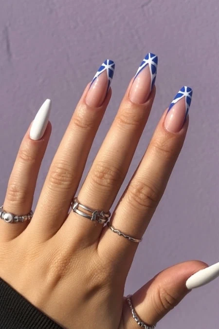 Bright blue and white geometric nail art design on well-manicured natural nails, featuring matte white accent nails, on a woman's hand with silver rings, against a purple background, for trendy nail fashion.