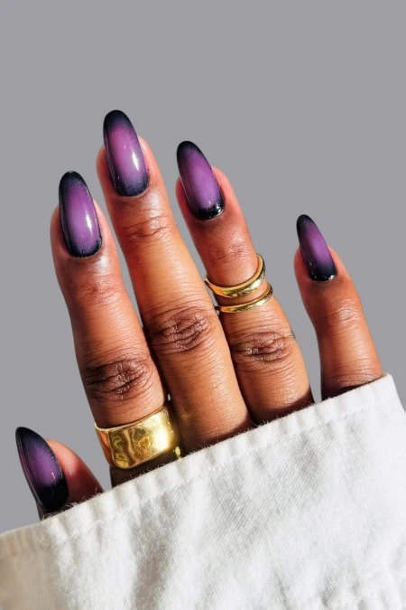 Vibrant purple and black ombre nail design on well-manicured fingers, showcasing trendy nail art. Perfect for beauty and fashion enthusiasts seeking stylish nail inspiration.