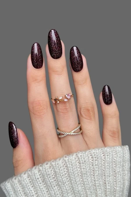 Deluxe dark purple glitter nail polish on perfectly manicured feminine nails with stylish rings, showcasing beauty and elegance for a stunning look.