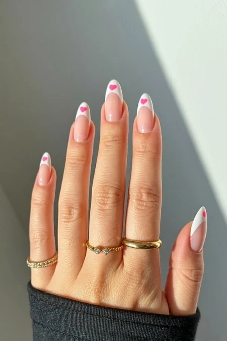 Beautiful manicured nails with white French tips and pink heart accents, showcasing trendy nail art and elegant jewelry. Perfect for a stylish, feminine look.