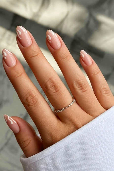 Elegant nude manicure with white drip nail art on natural nails, styled with a delicate silver ring, perfect for beauty and nail art enthusiasts.