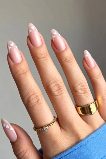 Delicate natural pink manicure with white heart accents on nails, stylish gold rings, and a blue sleeve. Perfect for a fresh, romantic, and elegant look. Ideal for beauty and nail art enthusiasts.