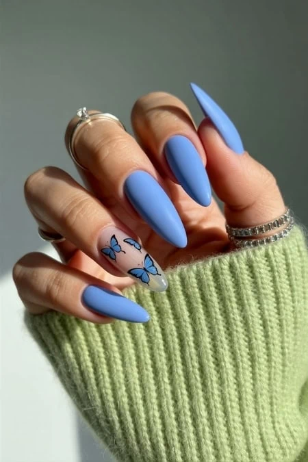Long blue coffin-shaped acrylic nails with butterfly nail art and silver rings on fingers, styled with a cozy green sweater. Perfect for beauty, nail art, and manicure inspiration.