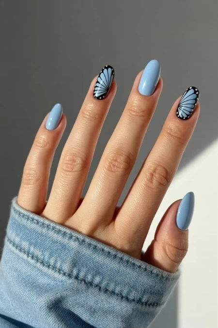 Delicate blue butterfly nail art on pastel blue manicure, perfect for spring and summer beauty trends, featuring glossy finish and intricate wing design on ring and middle fingers.