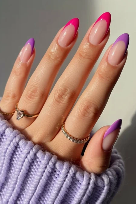 Vibrant pink and purple French manicure on natural nails with stylish rings, showcasing trendy nail art and jewelry for a chic, modern look.