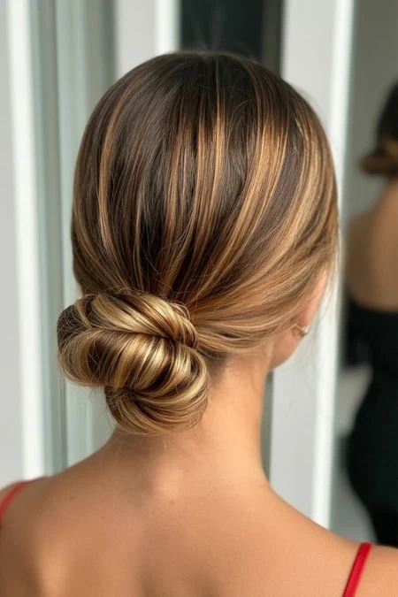Elegant low bun hairstyle with subtle highlights, perfect for a sophisticated look; suitable for weddings, events, or professional settings. Beautifully styled hair showcasing modern updo hair artistry.