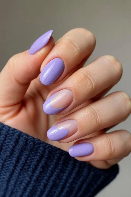 Vibrant lavender and nude gel nail polish manicure, perfectly shaped and glossy, on a woman's hand with a cozy navy blue sweater.