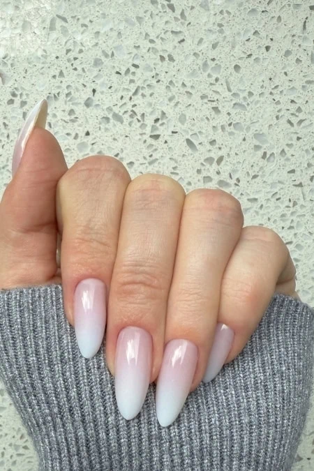 Delicate white ombre gel manicure on well-manicured nails with gray sweater, ideal for nail art, beauty, and cosmetics enhancements.