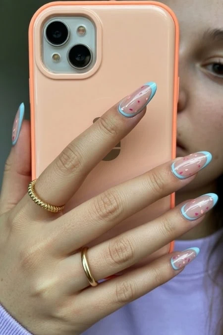 Colorful gel nail polish manicure with trendy almond-shaped nails on a woman's hand holding a peach-colored smartphone.