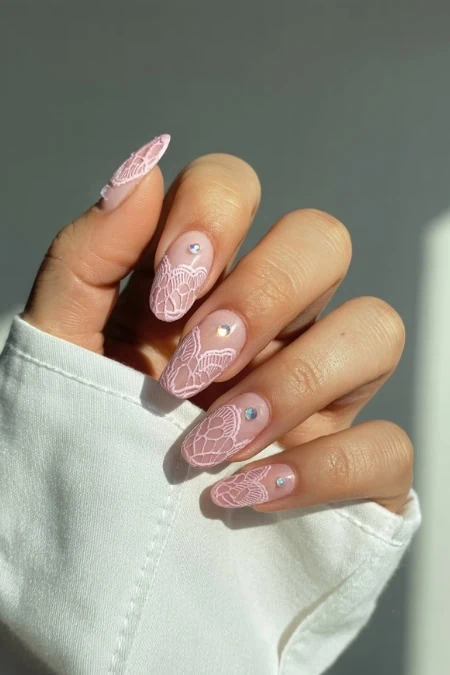 Delicate pink lace nail art with rhinestone accents on manicured nails, stylish and elegant nail design perfect for special occasions or everyday sophistication.