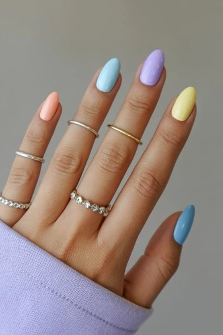 Colorful pastel gel nail polish manicure with rings on fingers, showcasing trendy spring nail designs and accessories for beauty and self-care.