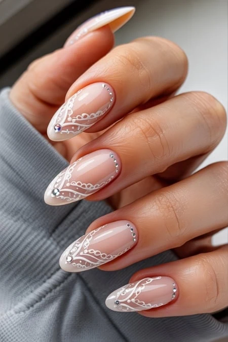 Elegant white and nude nail art with intricate lace design and rhinestone accents, perfect for a sophisticated beauty and manicure look.