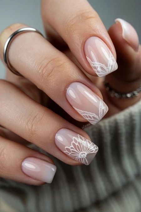 Elegant nude manicure with white floral nail art design, showcasing intricate nail artistry for a sophisticated beauty look.