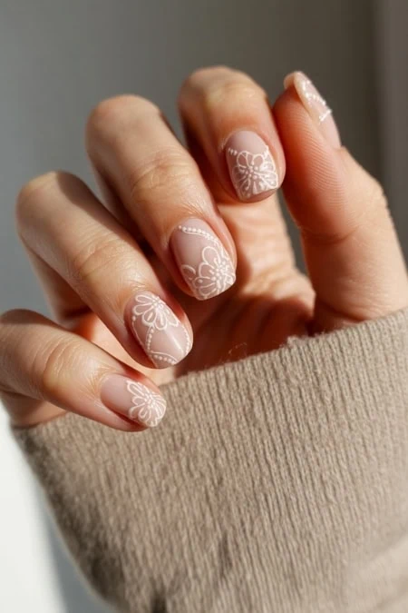 Delicate floral nail art with intricate white designs on natural nails for a chic, feminine look. Perfect for spring or special occasions, showcasing professional manicure art.