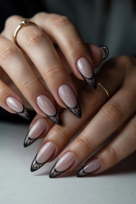 Elegant nude and black lace nails on manicured hands with gold rings, showcasing sophisticated and trendy nail design for beauty and fashion enthusiasts.