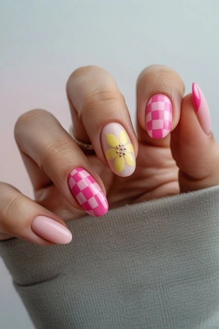 Bright pink and yellow floral nail art with checkered and solid designs on feminine manicured nails, showcasing creative nail art ideas for spring or summer.