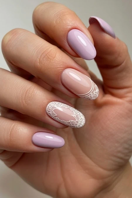Elegant pastel purple and nude nail art with intricate white lace design on ring finger, showcasing professional manicure and nail art creativity for beauty and fashion enthusiasts.