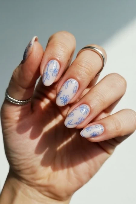 Delicate floral nail art with blue flower designs on white nail polish, perfect for spring or summer styles, showcasing trendy and elegant manicure ideas.