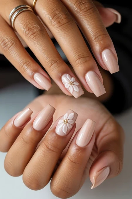 Elegant nude manicure with 3D floral nail art featuring white flowers and gold accents, perfect for a sophisticated and trendy nail look.