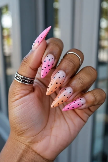 Colorful ombre stiletto nails with black polka dots, featuring pink, peach, and nude gradient shades, perfect for trendy nail art and sleek spring or summer manicure designs.