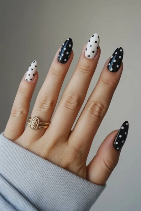 Polka dot nail art with black and white polish on long stiletto nails, trendy manicure design for fashionable women.