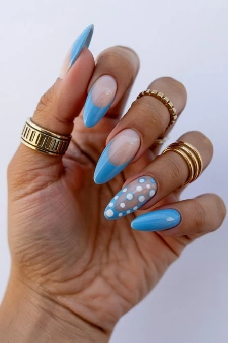 Vibrant blue and white manicure with polka dot accent nails, featuring gel nails, stylish gold rings, and intricate nail art, perfect for beauty and fashion enthusiasts.