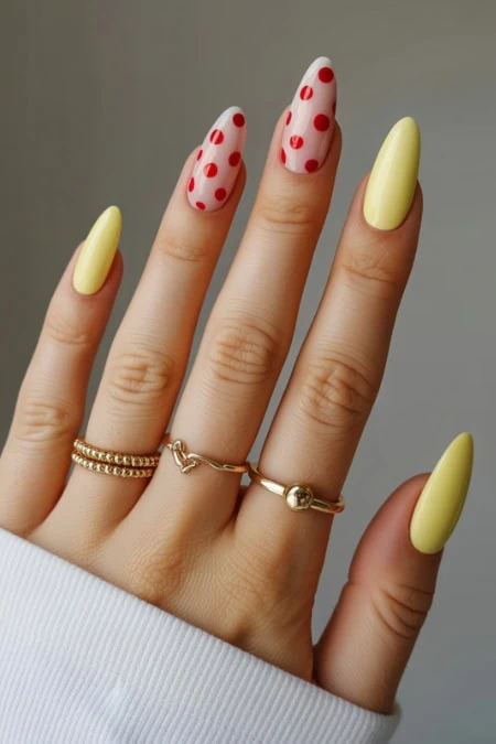 Bright yellow and red polka dot nail art on well-manicured fingers, showcasing trendy and chic manicure design with layered gold rings for added style and elegance.