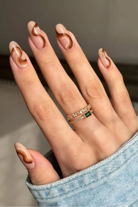 Elegant manicured nails with a glossy, nude and caramel swirl design showcasing trendy nail art and skincare.