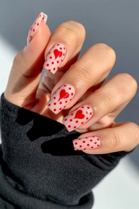 Bright Valentine's Day nail art with red hearts and polka dots on a soft pink base, featuring creative nail design, perfect for special occasions and expressing love.