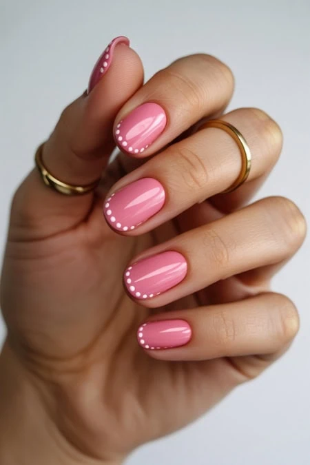 Pink manicured nails with white dotted accents, showcasing elegant nail art and trendy beauty styles for a polished look.