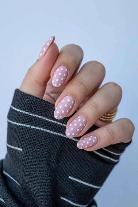 Soft pink nails with white polka dots on well-manicured fingers, showcasing trendy nail art and stylish manicure for beauty and self-care.