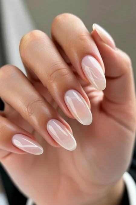 Elegant nude almond-shaped manicure with subtle white marble accents, perfect for a sophisticated and trendy beauty look.