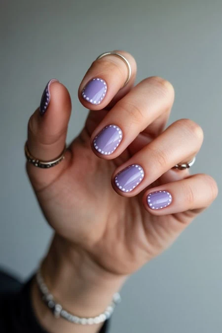 Hand with lavender manicure featuring white dotted nail art, showcasing sleek, stylish nail designs perfect for beauty and self-care.