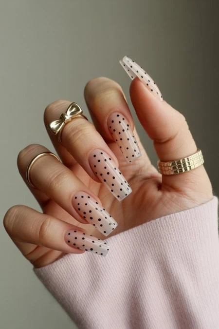 Polka dot nude gel nail design with gold rings, trendy and stylish manicure, perfect for fashion-forward nail art, on well-groomed fingers with long acrylic nails.