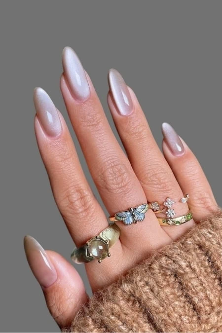 Elegant manicure with glossy nude nails and stylish rings featuring butterflies, flowers, and gemstones, showcasing chic jewelry aesthetics for a sophisticated fashion look.