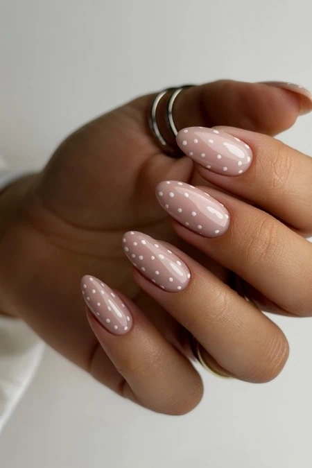 Polished almond-shaped nails with pink base and white polka dots, perfect for stylish nail art and beauty trends.