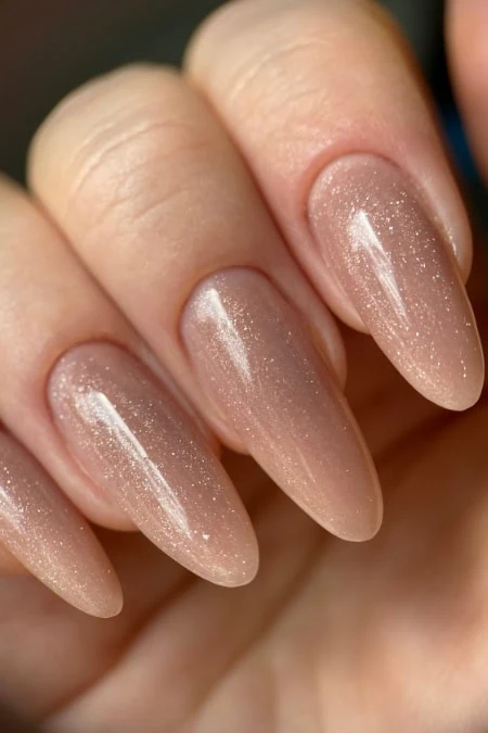 Elegant nude glossy nail polish with subtle shimmer on almond-shaped nails, perfect for a natural yet sophisticated look.