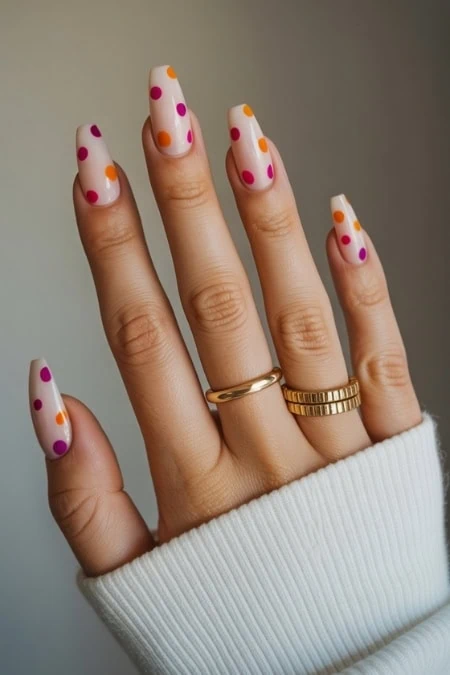 Colorful polka dot nail art on manicured fingers with gold rings, perfect for spring or summer trendy manicure, on a natural background.