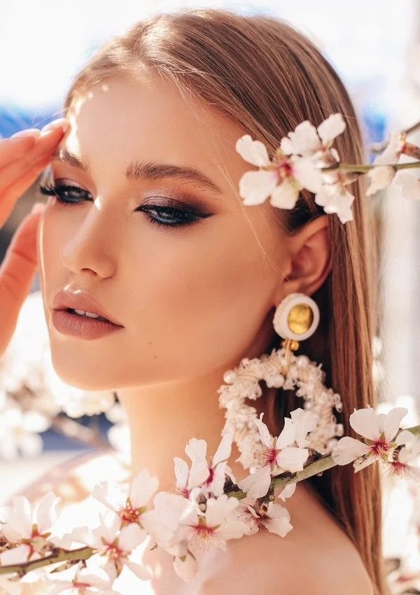 Elegant woman with flawless makeup and jewelry surrounded by cherry blossoms, embodying beauty and style for skincare and cosmetic inspiration.