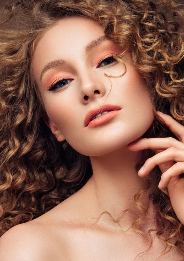 Vibrant woman with curly hair and flawless makeup, close-up portrait highlighting natural beauty, skincare, and hair care tips from The Beauty Deep Life website.