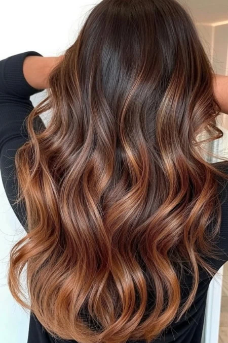 Beautiful long wavy hair featuring rich brown tones blended with caramel highlights, styled with soft waves for a glamorous and healthy appearance.