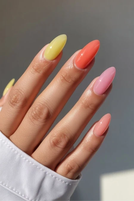 Elegant pastel nail polish manicure with yellow, coral, and pink shades on well-groomed fingers.