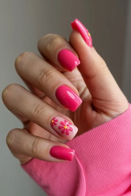Pink floral nail art, manicured nails, and vibrant pink polish on fingers with a pink sleeve.