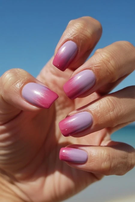 Nail art featuring pink and purple ombre gradient on well-manicured nails against a clear blue sky background. Perfect for showcasing trendy, colorful nail designs and beauty tips.