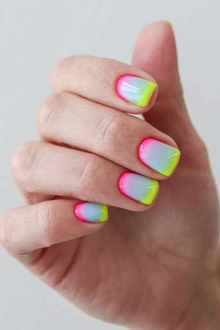 Neon gradient nail design featuring vibrant pink, yellow, and blue colors on well-manicured nails, perfect for summer or special occasions.