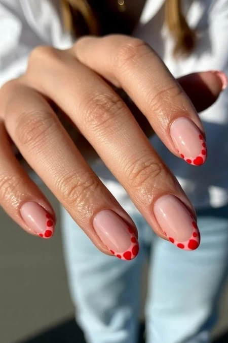 A woman's hand showcasing a fresh manicure with natural nails and red polka dot nail art on the tips, highlighting trendy Summer nails.