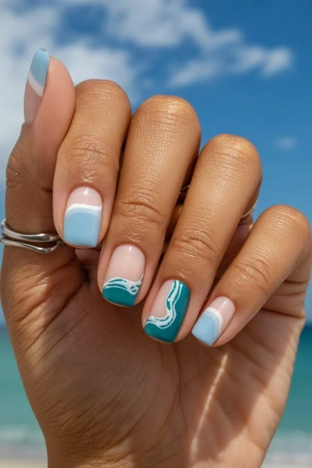 Inspired nail art with blue and white wave patterns on manicured nails, set against a clear sky and ocean background. Perfect for summer, vacation, and beauty enthusiasts.