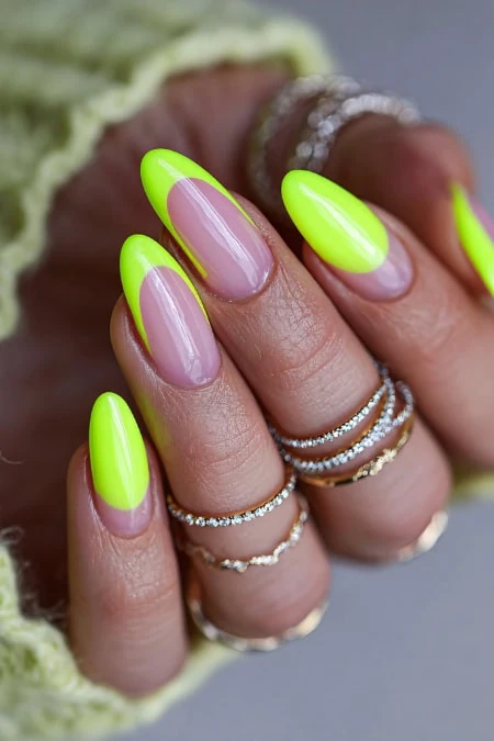 Vibrant neon green and nude manicure with almond-shaped nails, accessorized with multiple silver rings, showcasing trendy and stylish nail design for beauty and fashion enthusiasts.