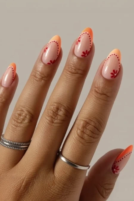 Up of a hand with beautifully manicured nails featuring peach-colored polish with red floral accents and dotted details, highlighting trendy nail art design for beauty lovers.