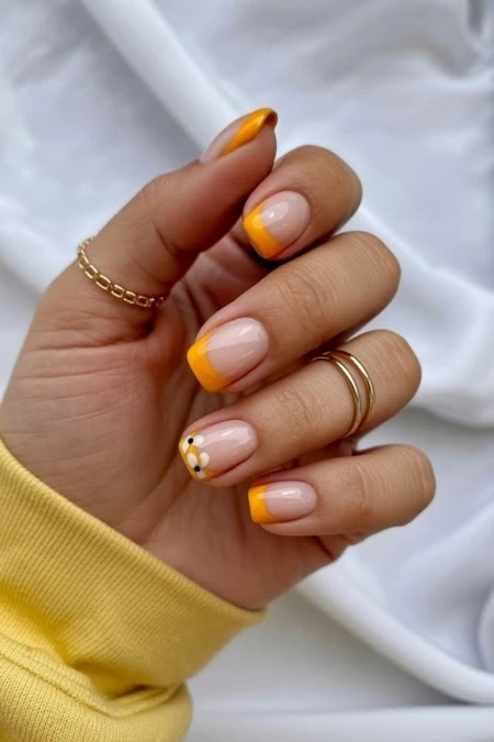 Yellow French manicure with floral accent nail, close-up of hand holding a white lipstick tube, on a soft white background.